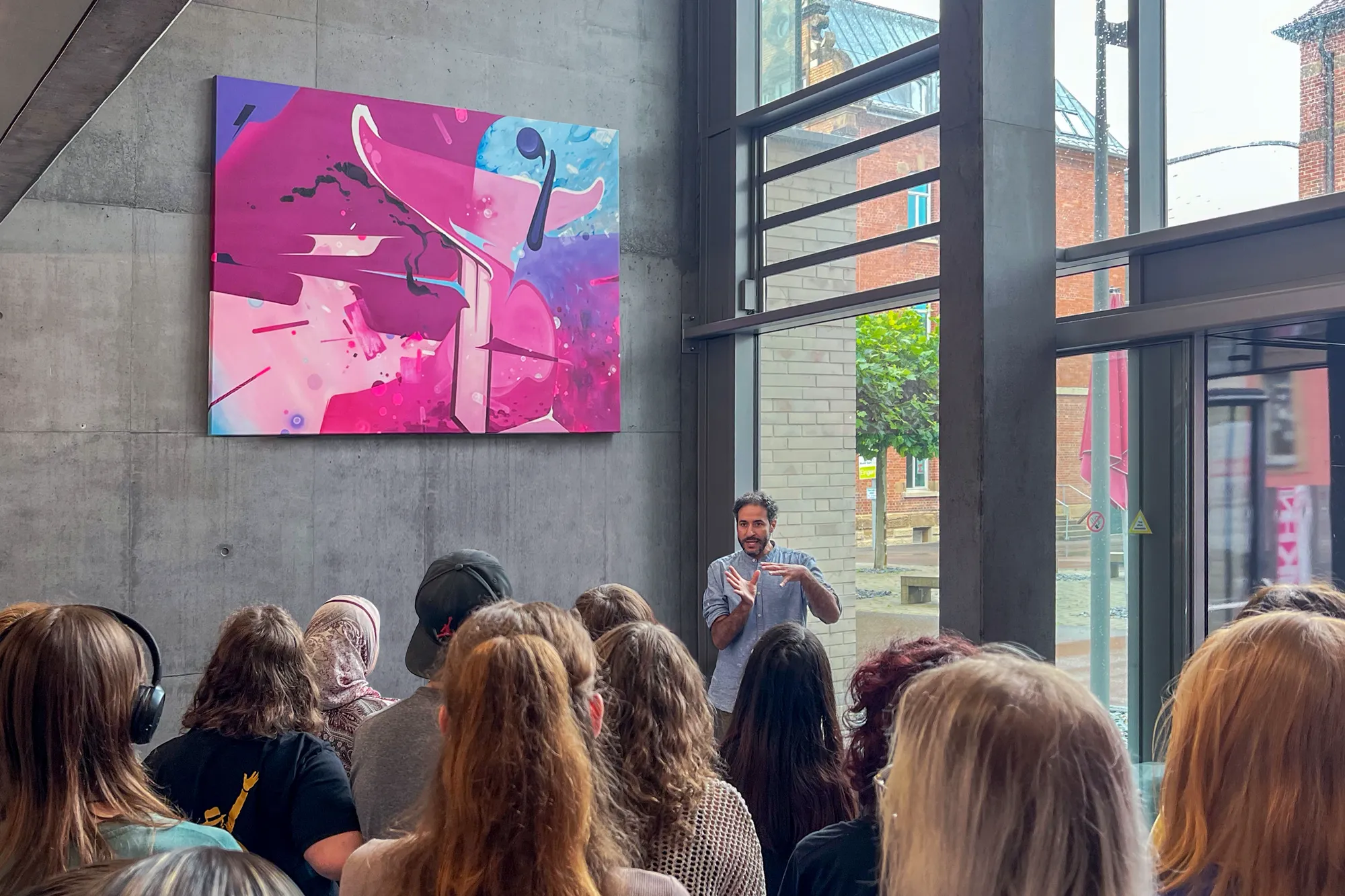 afk Heilbronn - Emin Hasirci vor eine Gruppe SchülerInnen, die ihm zuhören, während er sein Kunstwerk erläutert.